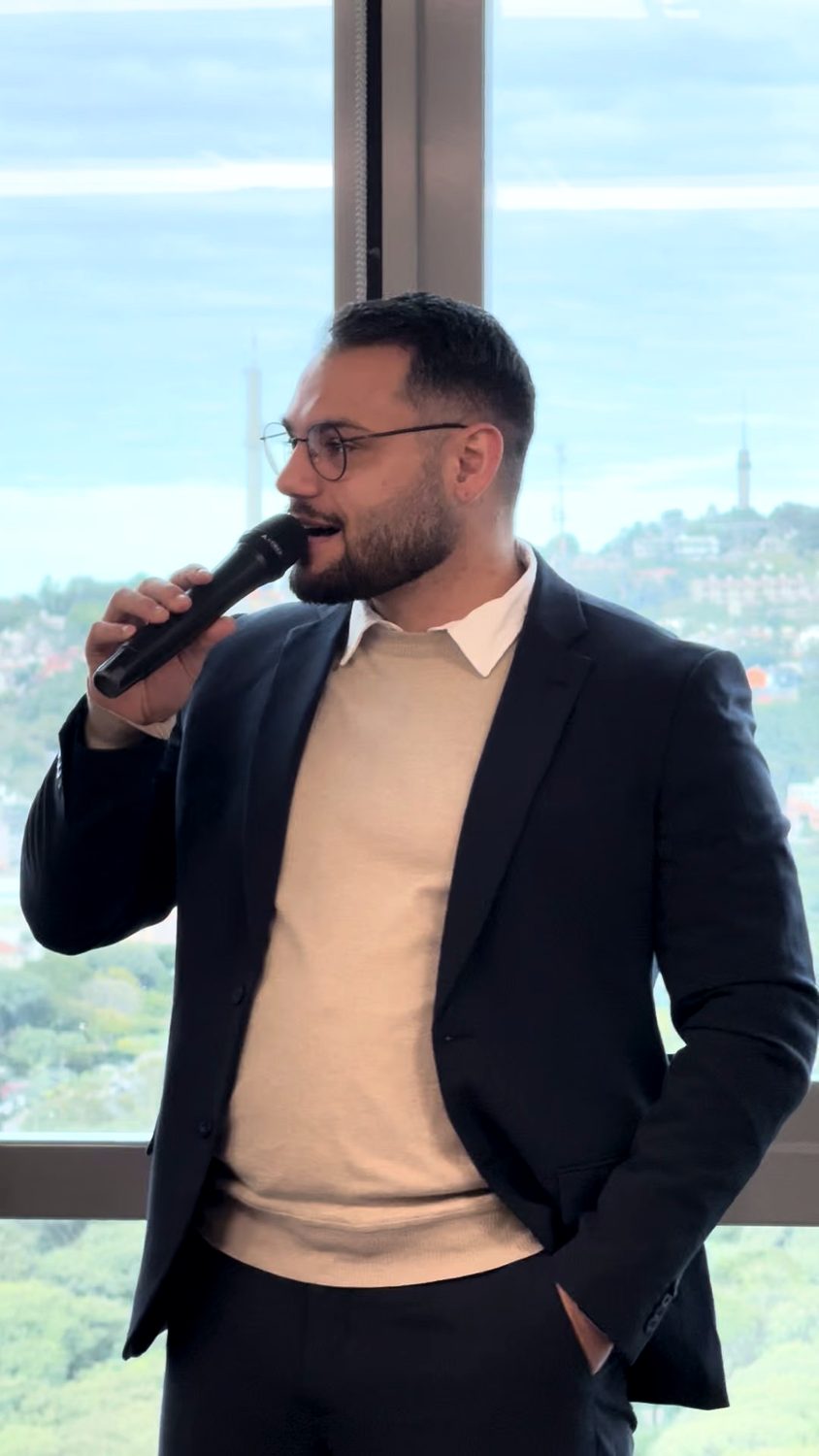 Matheus falando ao microfone diante de uma janela